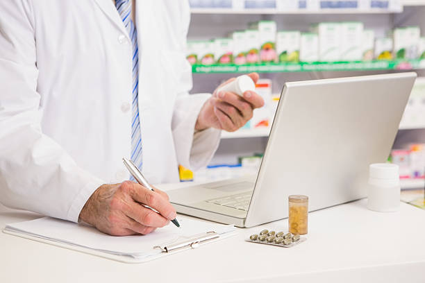 Pharmacist writing on clipboard and holding medication in the pharmacy Pharmacist writing on clipboard and holding medication in the pharmacy